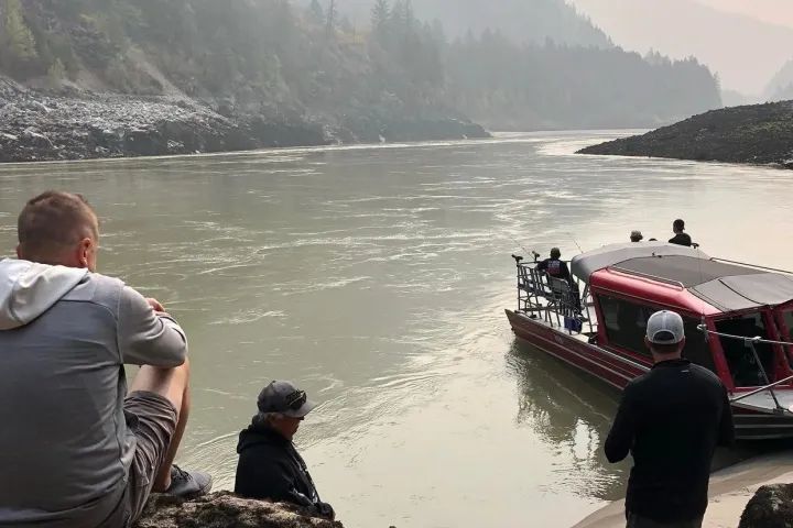 A group of people are sitting on a rock looking at a boat in the water.