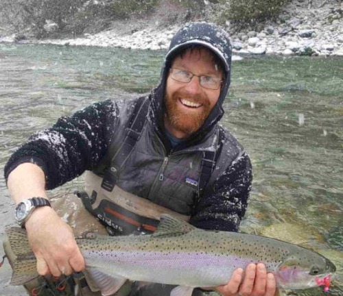 A man is holding a large rainbow trout in his hands.