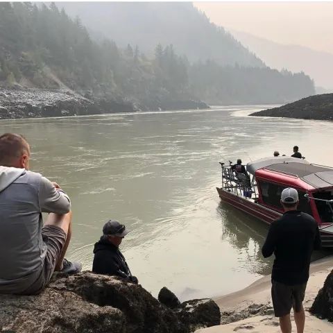 A man sits on a rock looking at a boat in the water
