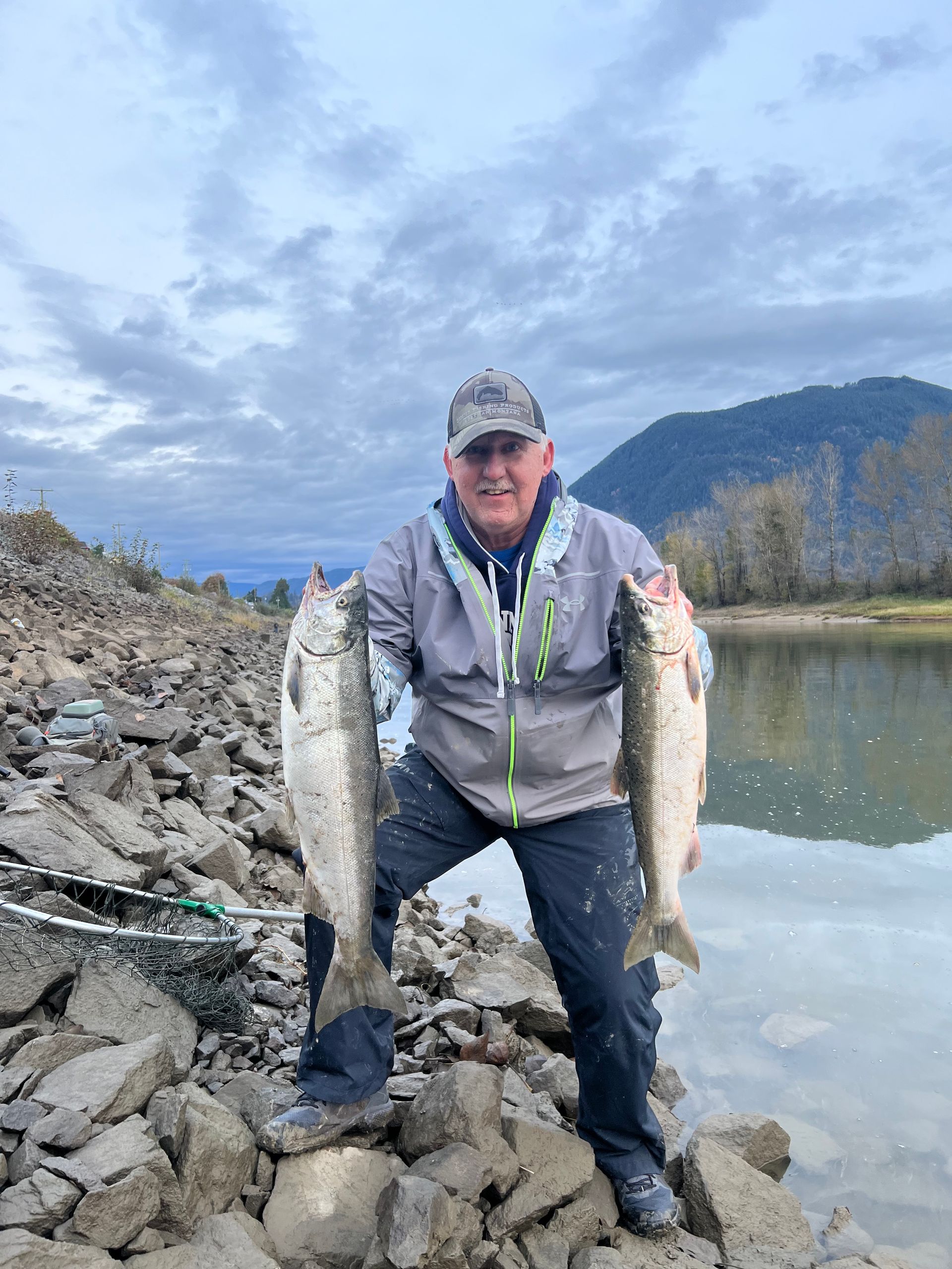 A man wearing a hat that says sgm is holding 2 large fish