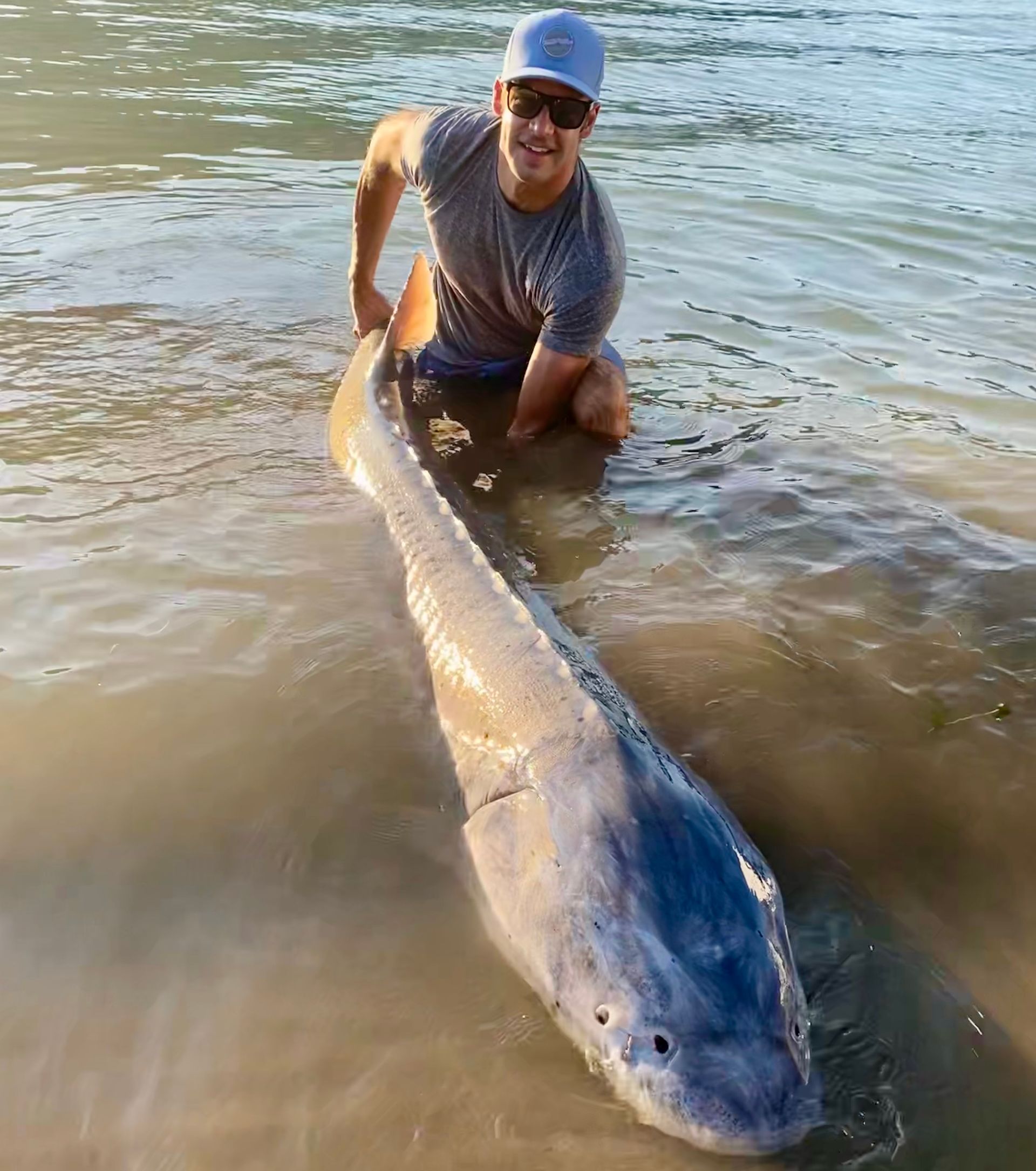 A man wearing a hat and a backpack is standing in front of a body of water.