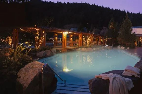 A large swimming pool is lit up at night with a bridge in the background.