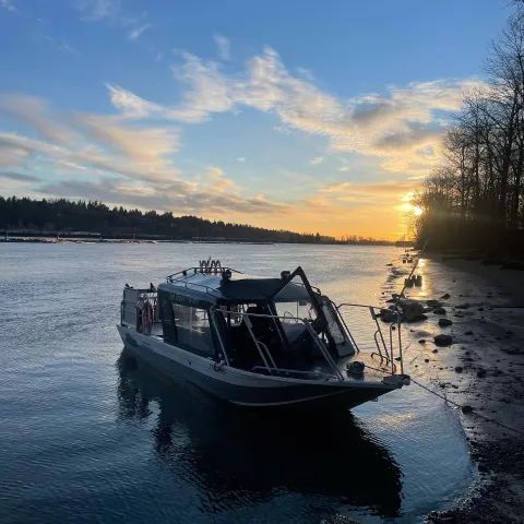 A boat is docked on the shore of a lake at sunset.