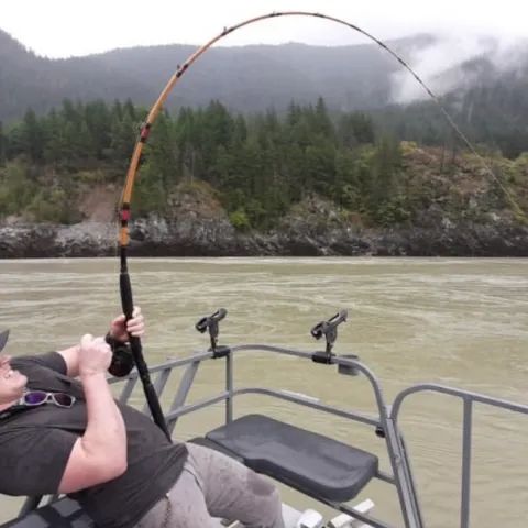 A man is sitting on a boat holding a fishing rod.