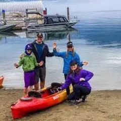 A group of people are standing next to a kayak on the beach.
