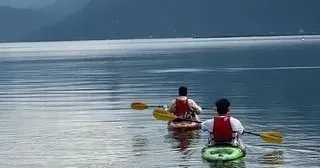 Two people are paddling kayaks on a lake.