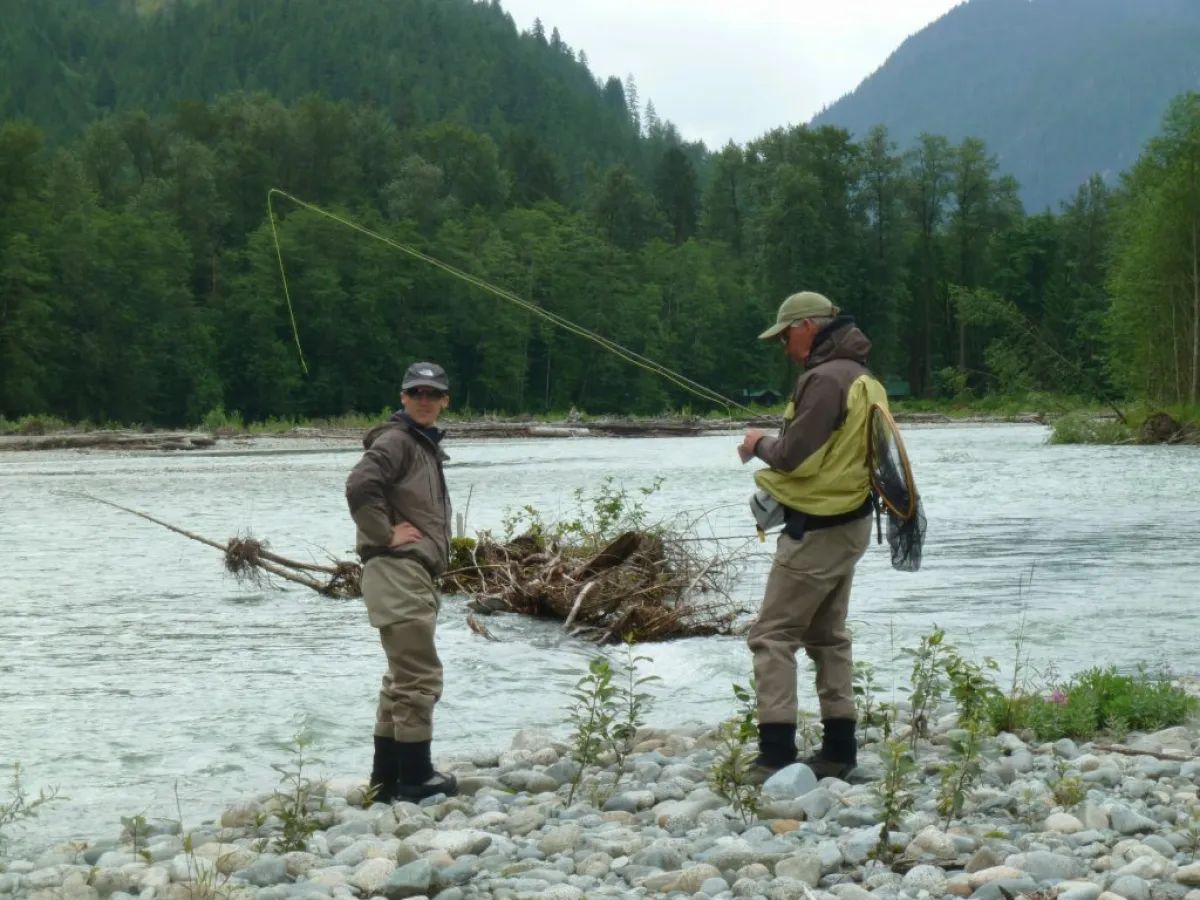 Two men are fishing in a river with mountains in the background