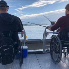 Two people in wheelchairs are fishing on a boat
