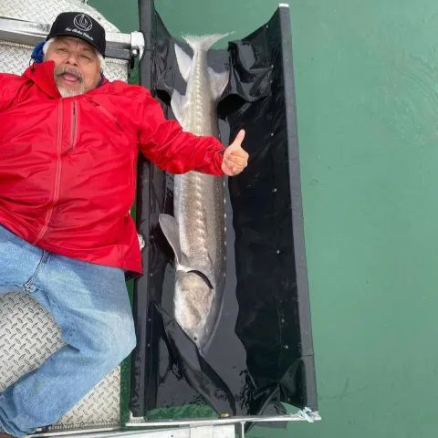 A man in a red jacket is giving a thumbs up next to a large fish