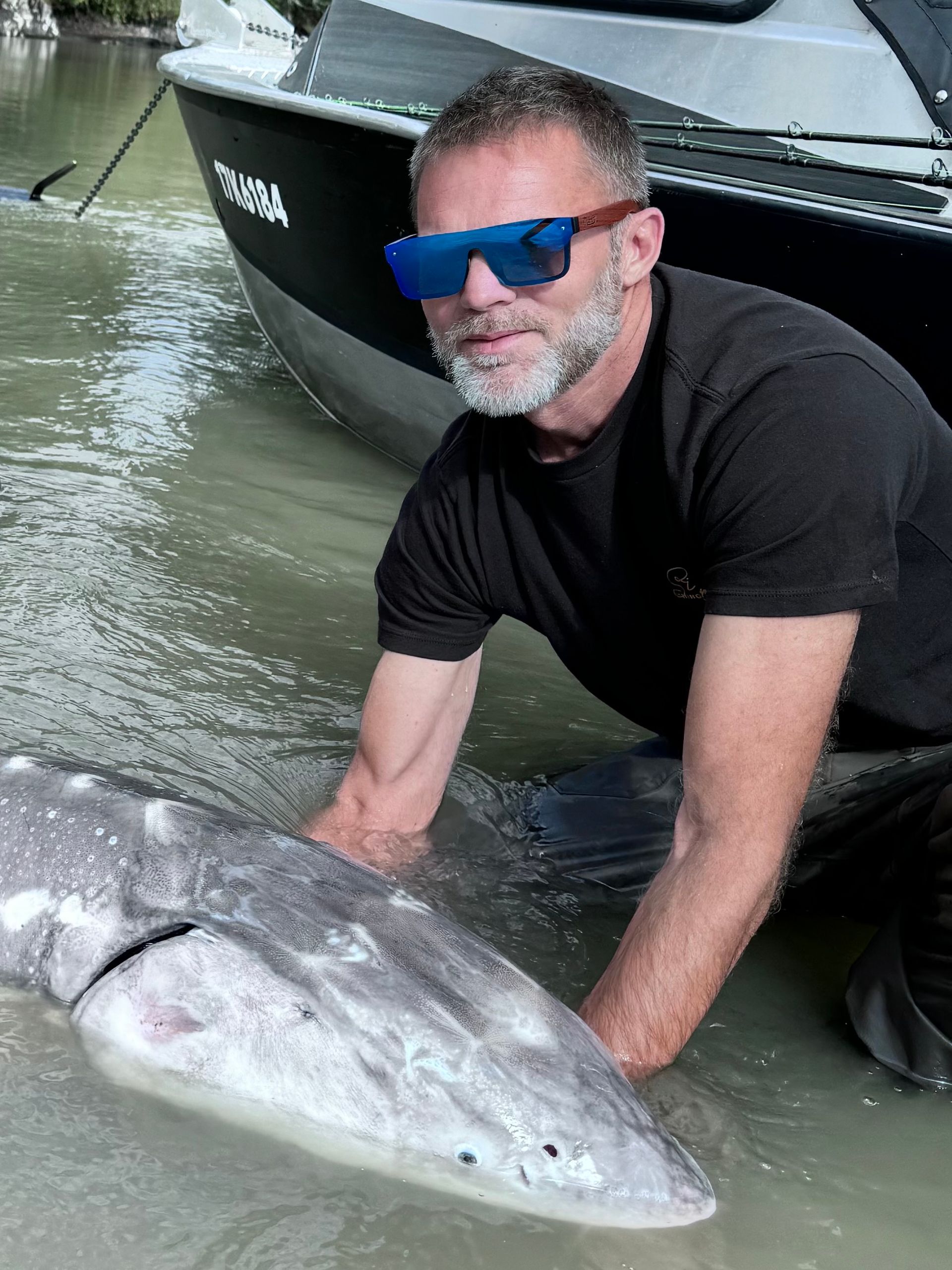A man wearing sunglasses in water with a sturgeon.