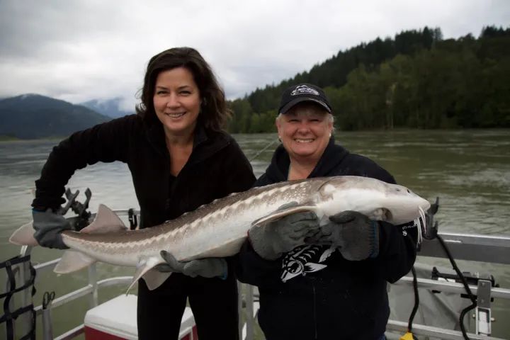 Two women are holding a large fish on a boat