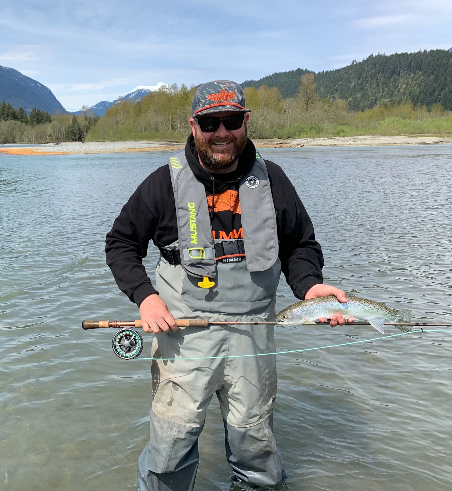Man standing in water with fishing rod and fish.