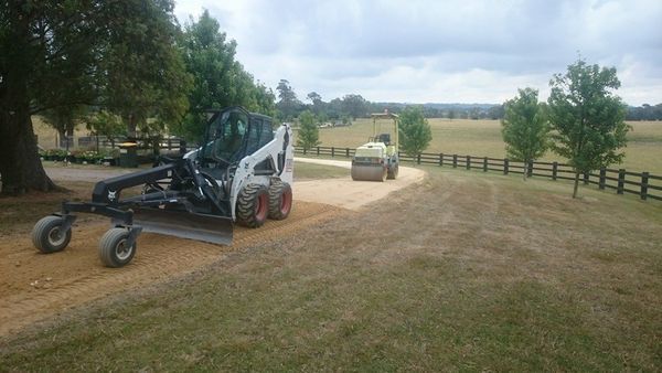 A bulldozer is driving down a dirt road next to a fence.