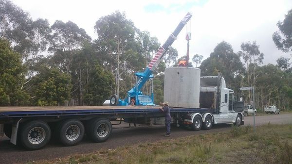 A man is standing next to a semi truck with a crane attached to it.