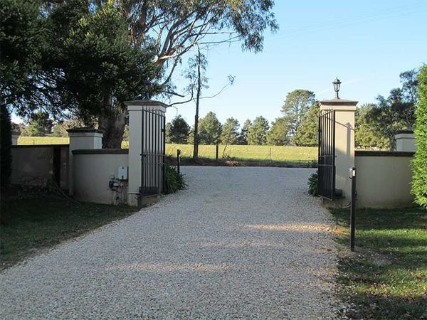 A gravel driveway leading to a gate with trees in the background