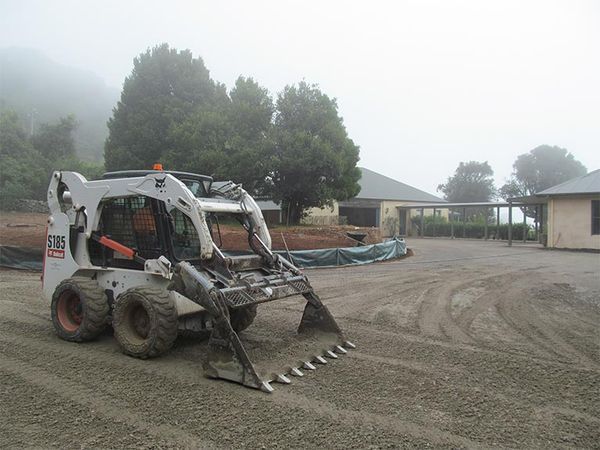 A bobcat is parked in a dirt lot in front of a house.