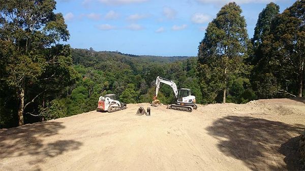 A couple of excavators are sitting on top of a dirt hill.