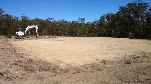 A white excavator is sitting in the middle of a dirt field.