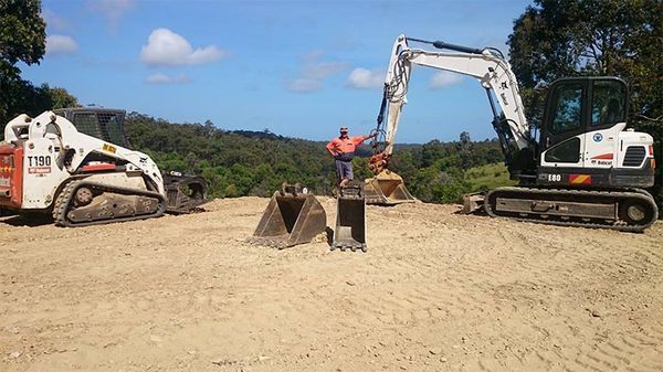 A man is standing next to a bulldozer in a dirt field.
