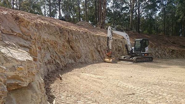 A bulldozer is driving down a dirt road next to a rock wall.