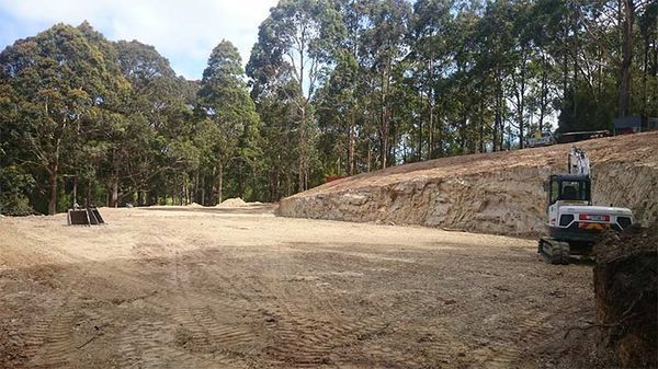 A large dirt field with trees in the background and a bulldozer in the foreground.