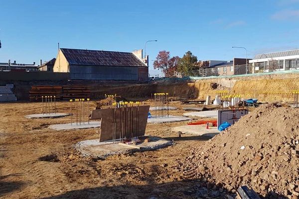 A construction site with a building in the background and a pile of dirt in the foreground.