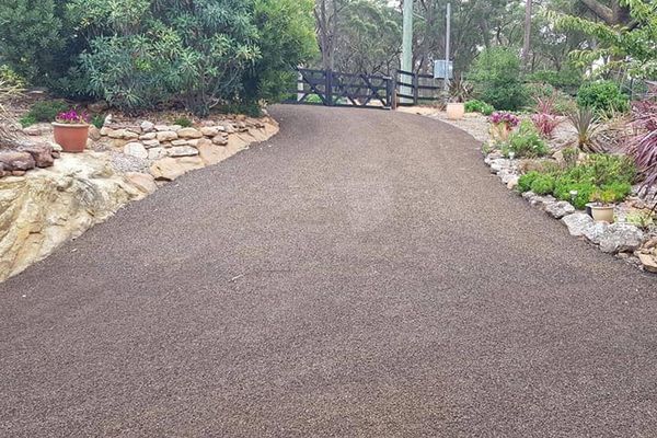 A dirt road leading to a wooden gate surrounded by trees and rocks.