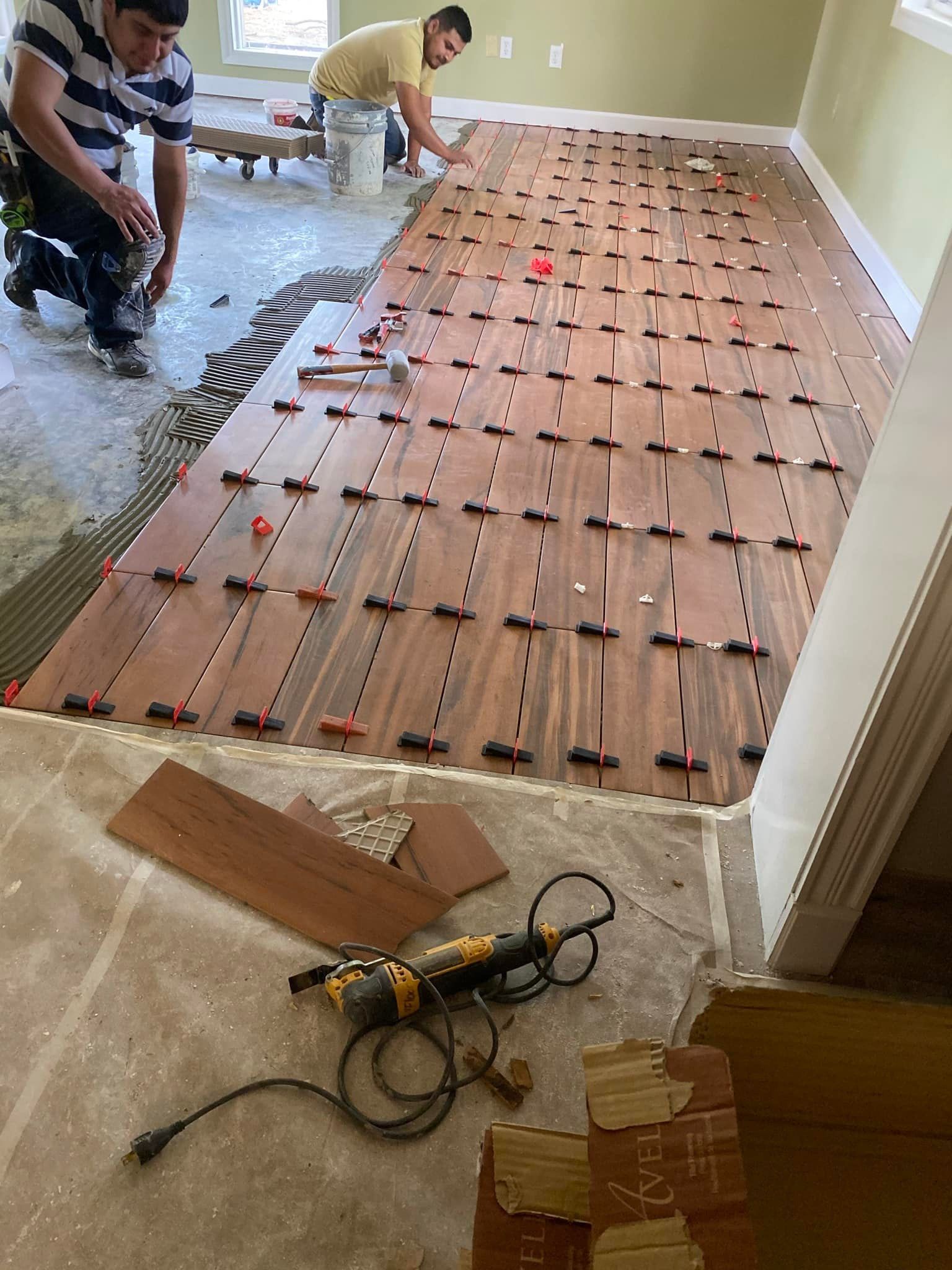 Two men are installing a wooden floor in a living room.