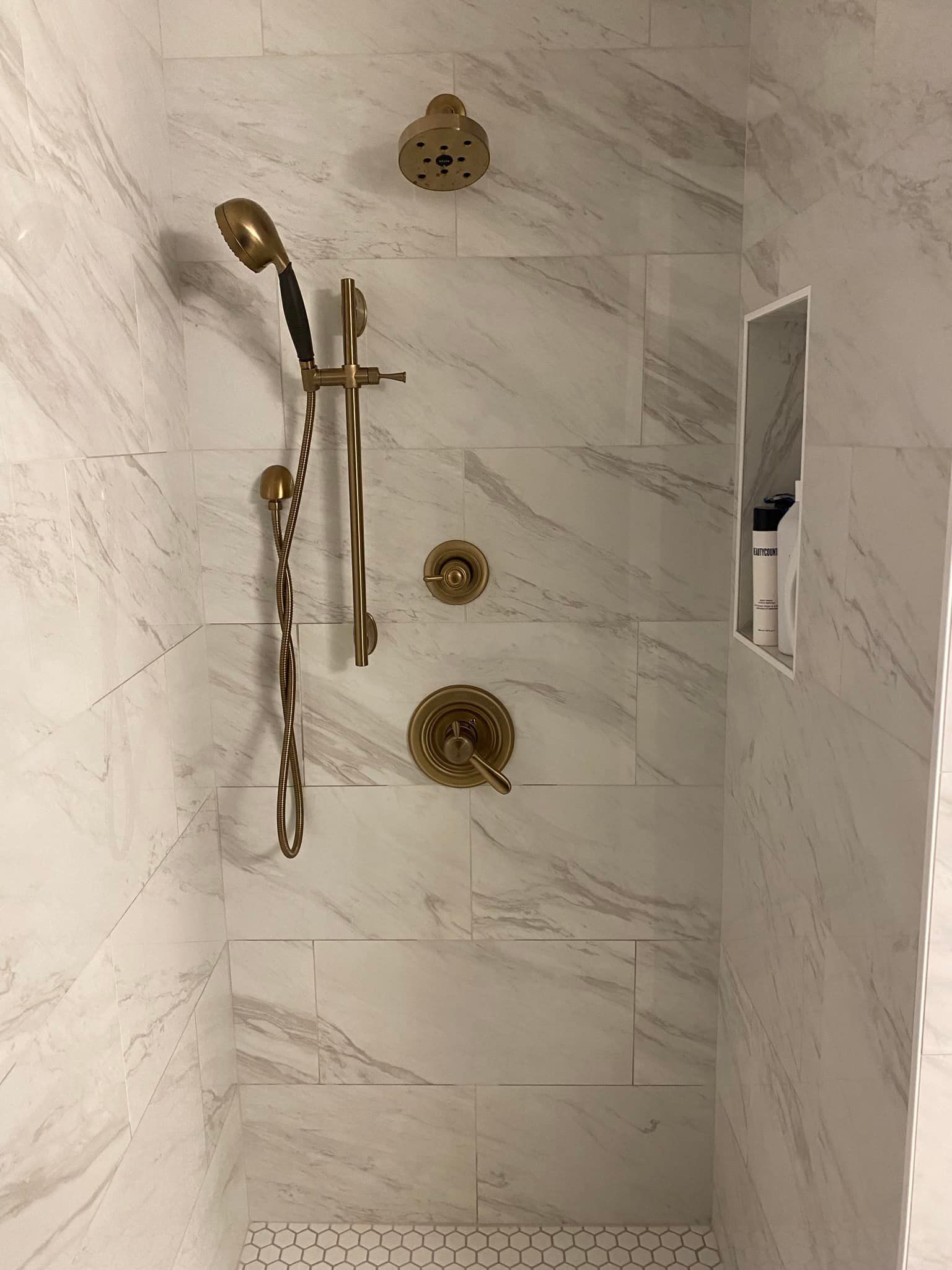 A shower with a marble wall and a gold shower head.
