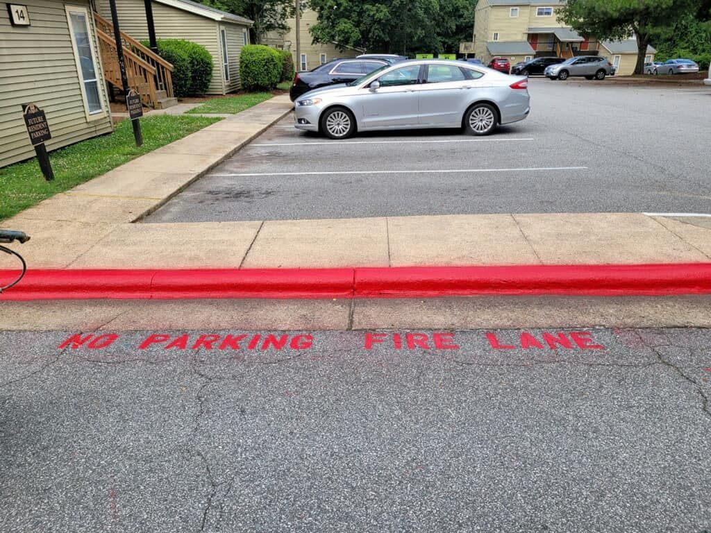 A silver car is parked in a parking lot next to a red curb.