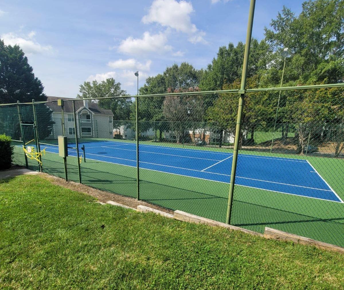 A tennis court with a fence around it and a house in the background