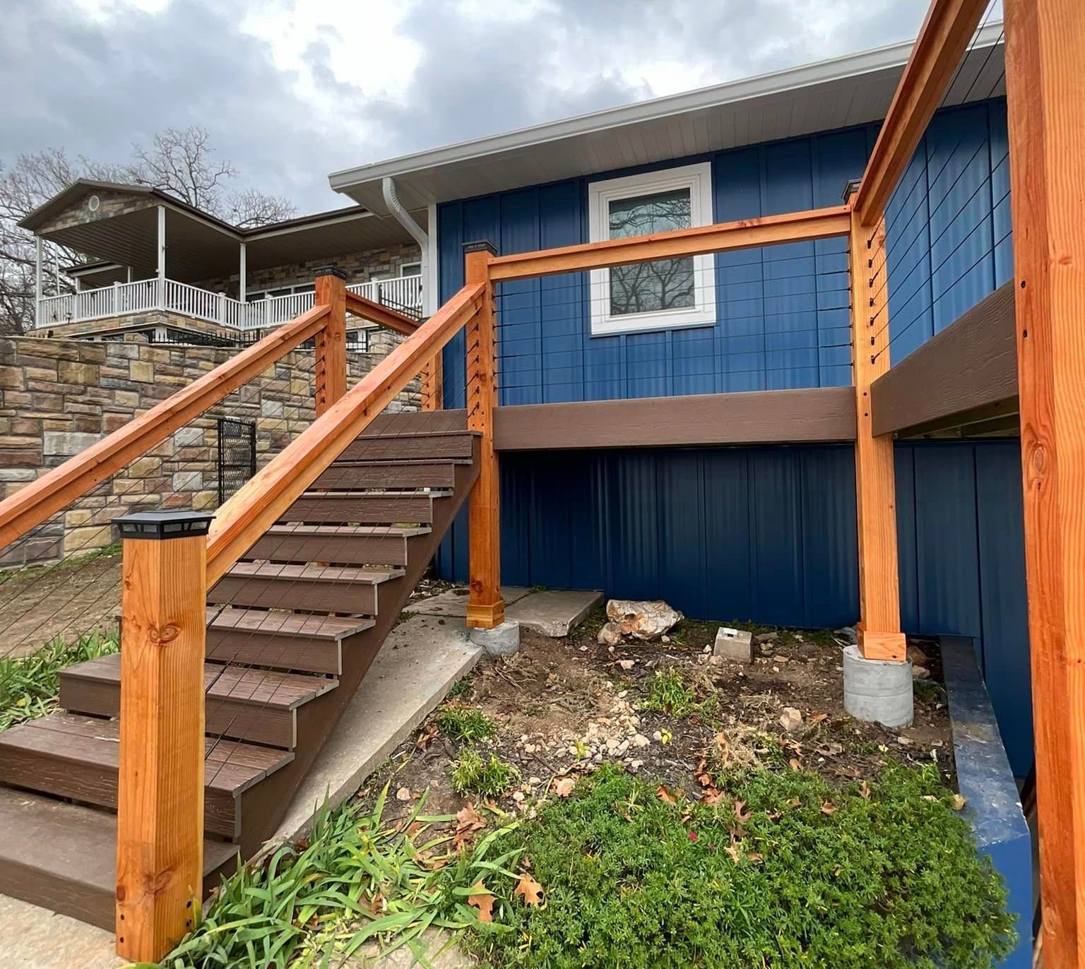 A blue house with a wooden deck and stairs leading up to it.
