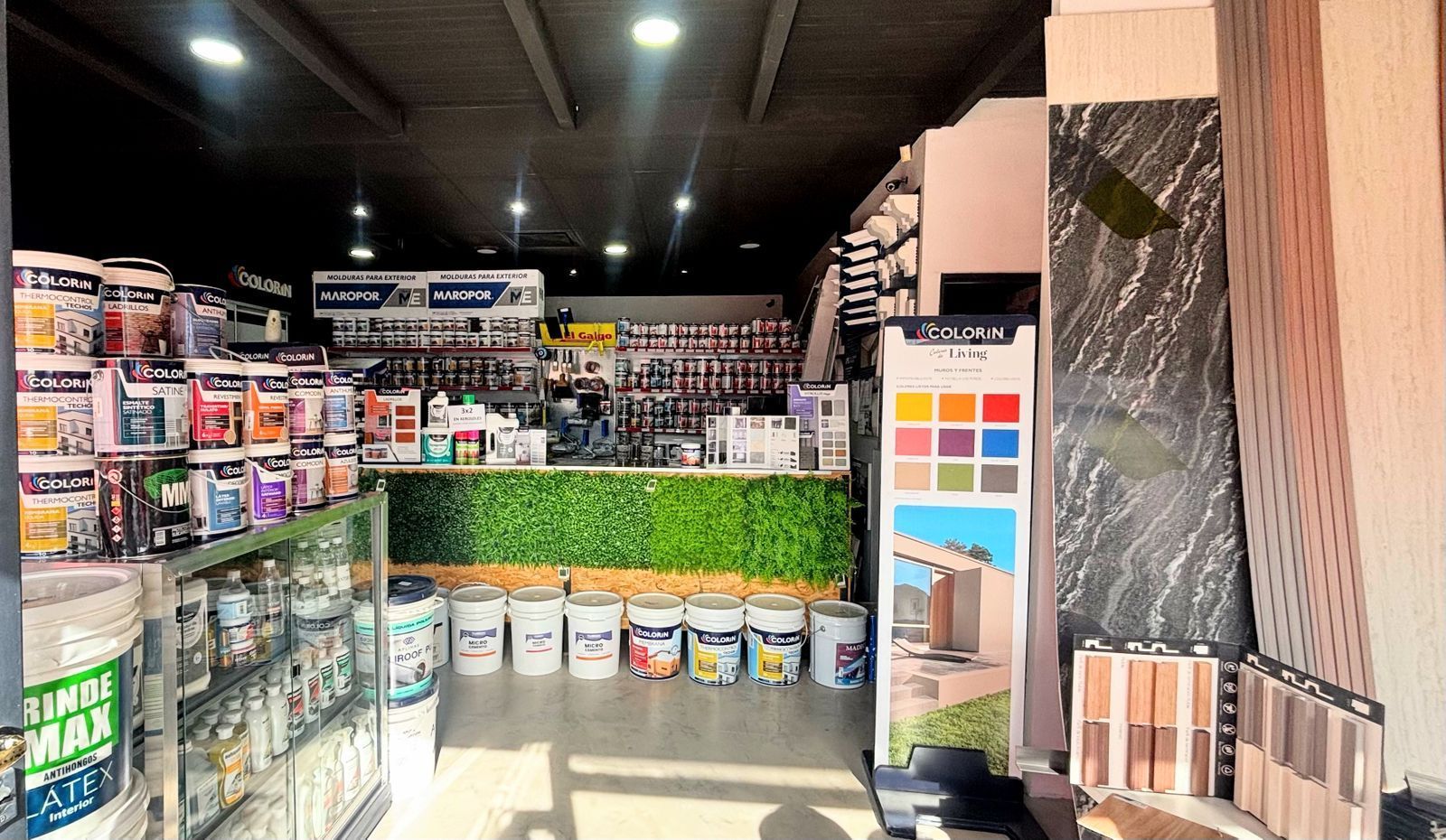 Interior de ferretería con pintura, herramientas y expositor, con detalles en las paredes verdes.