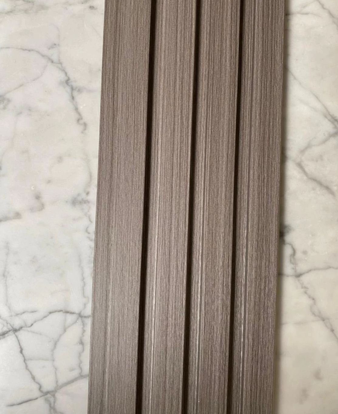 Cuatro tablones de madera con veta vertical de color marrón grisáceo, colocados sobre una superficie de mármol.