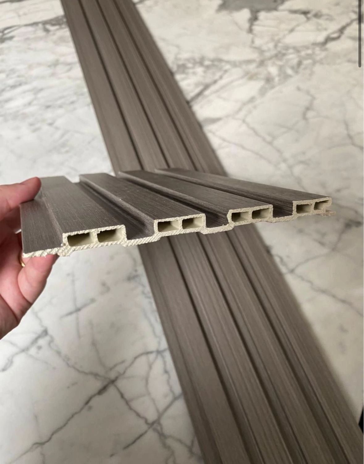 Cuatro tablones de madera con veta vertical de color marrón grisáceo, colocados sobre una superficie de mármol.