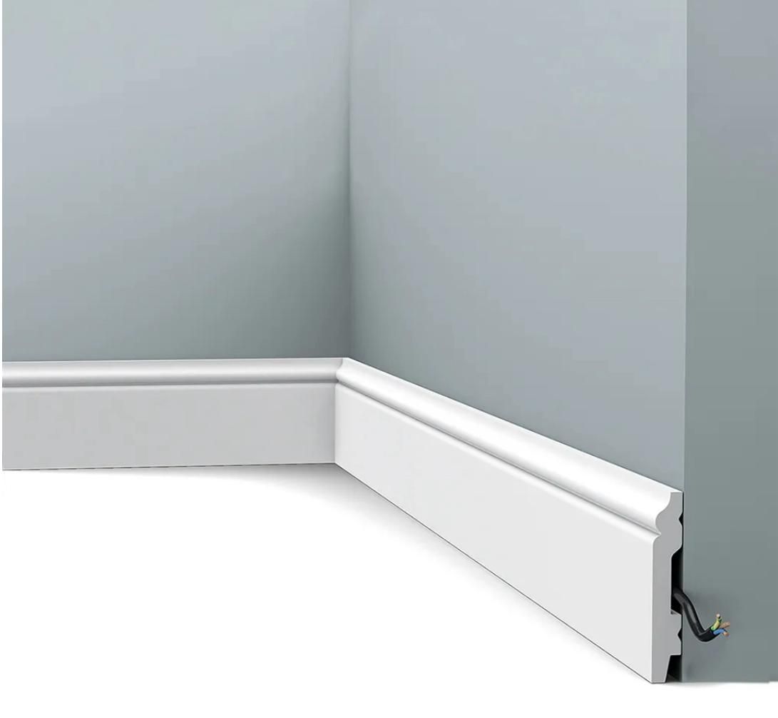 Moldura de zócalo blanca en una esquina de una habitación, con cables eléctricos visibles.