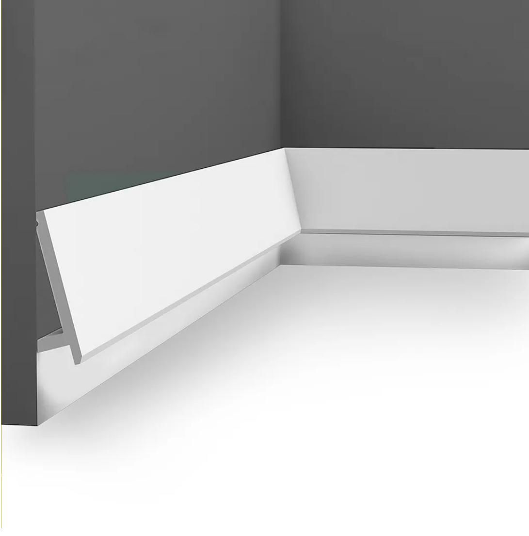 Moldura de zócalo blanca en una esquina, contra paredes grises y piso blanco.