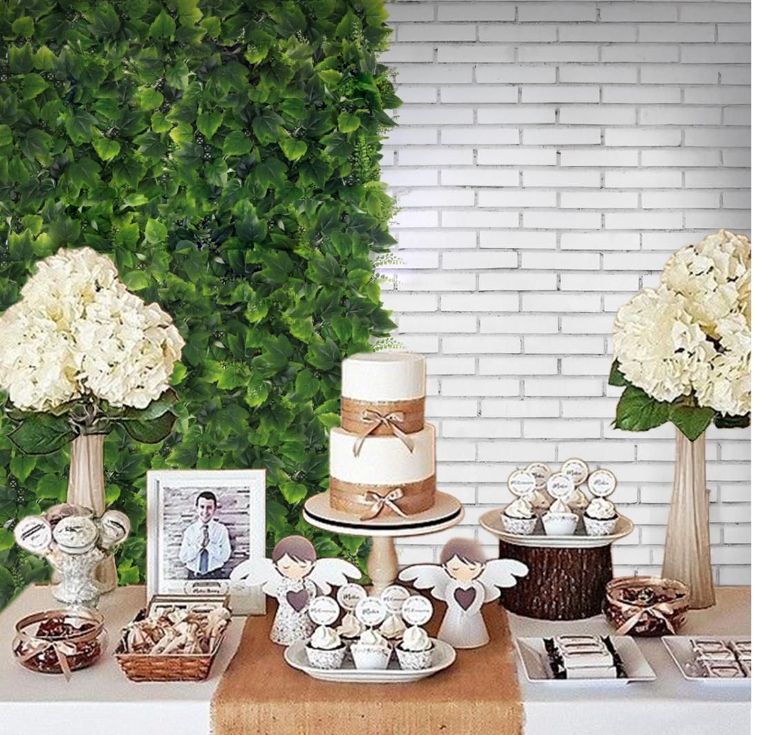 Mesa de postres con pastel de varios niveles, cupcakes y flores frente a una pared verde y ladrillo blanco.