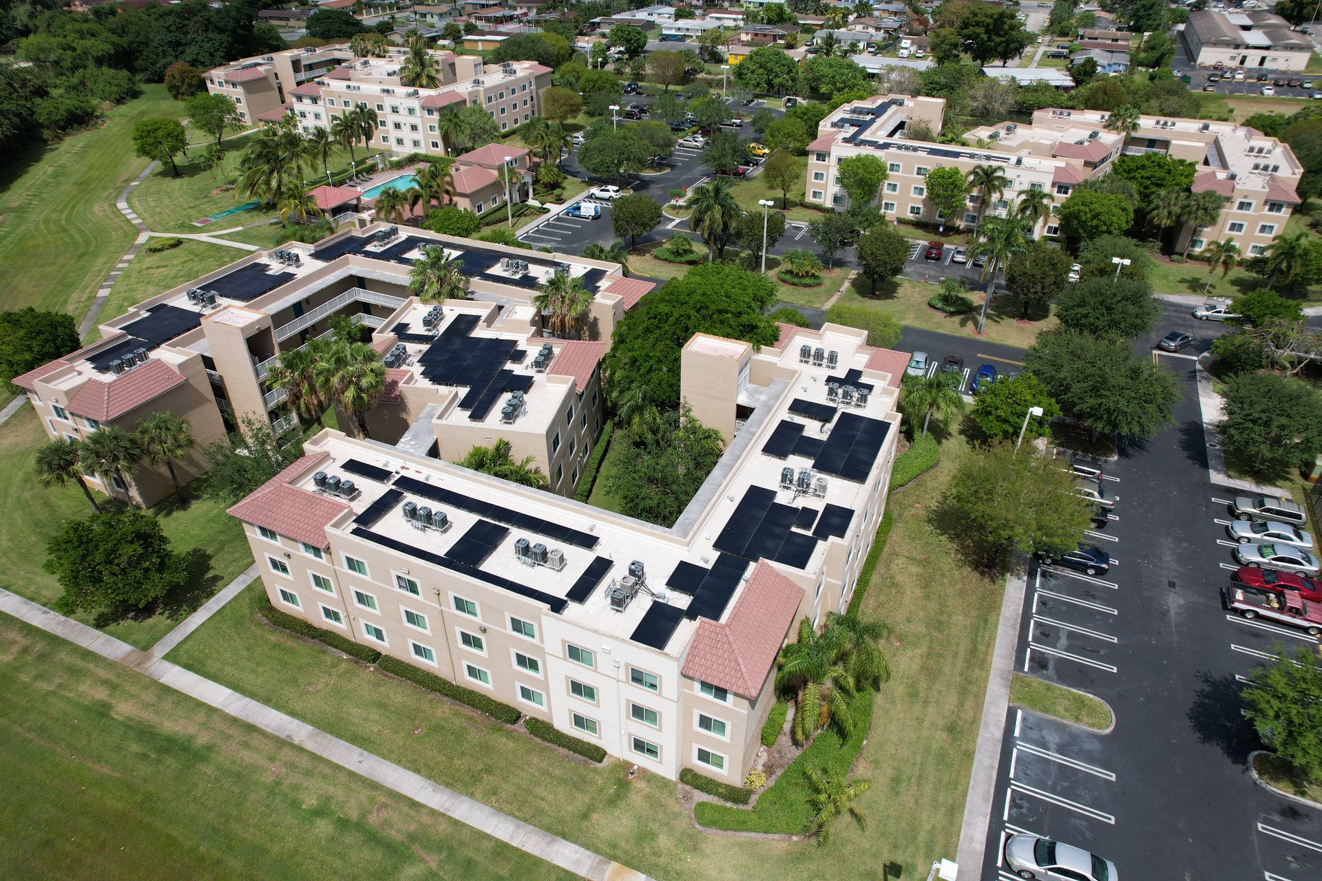 Aerial view of apartment buildings with solar panels, surrounded by green grass and a parking lot.