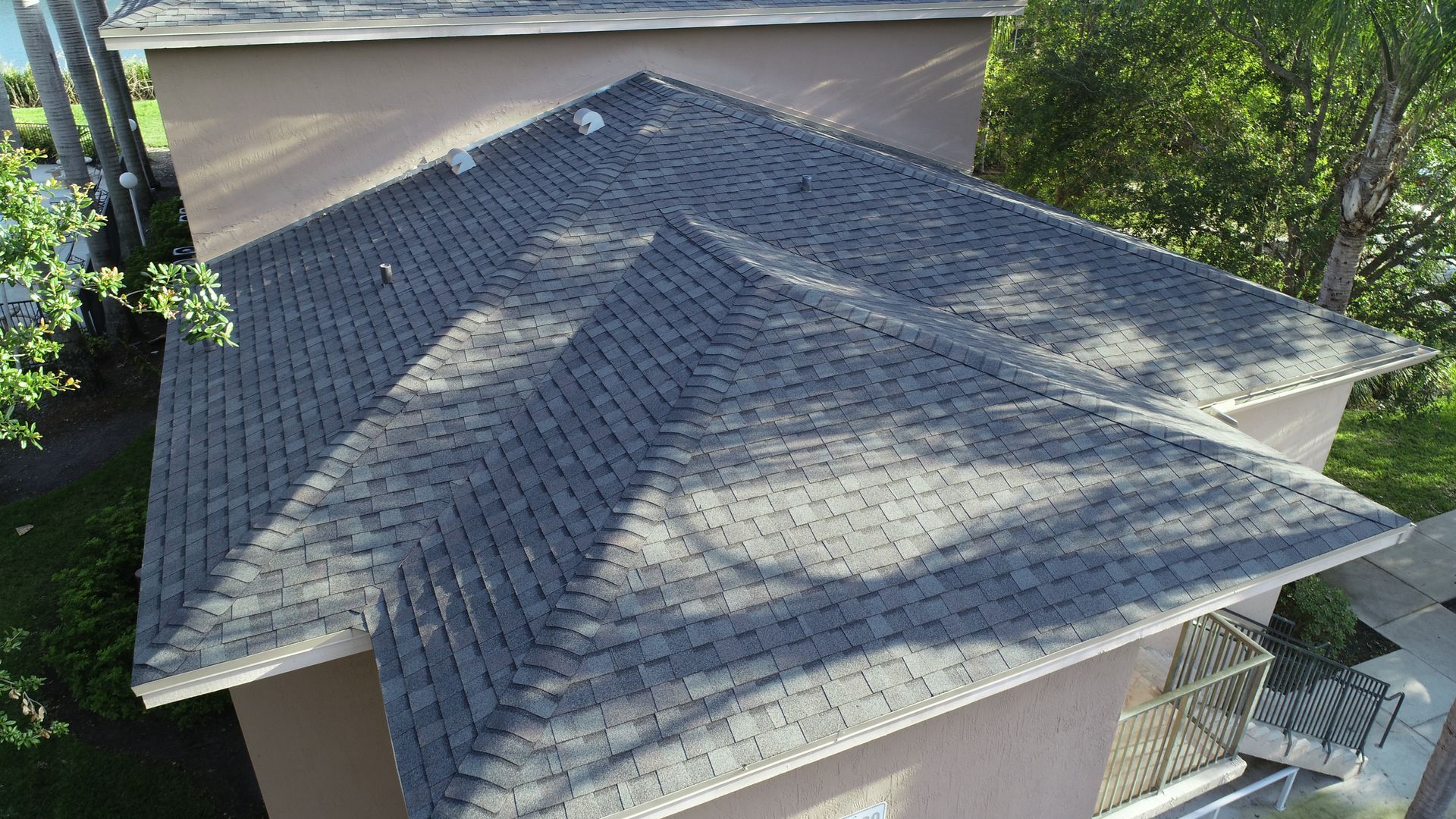 Gray shingle roof of a light brown building, seen from above on a sunny day.