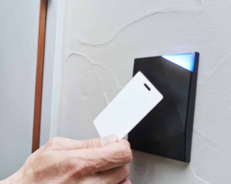Hand holding a white access card near a black card reader mounted on a textured white wall.