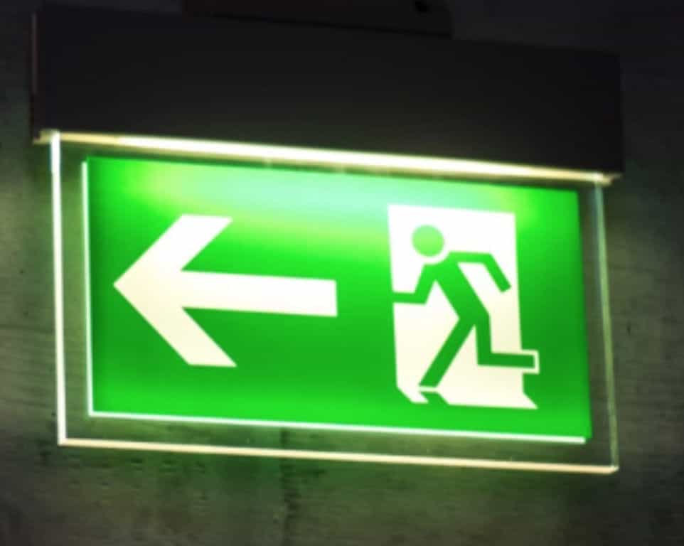 Green illuminated exit sign with a running person and arrow pointing left.
