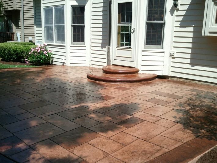 Brick-patterned, stained concrete patio with steps leading to a white house entrance. Shadows cast across the patio.
