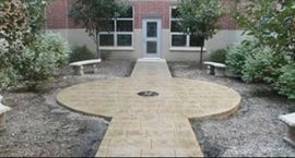 Stone patio with path leading to a building's door, flanked by benches and greenery.