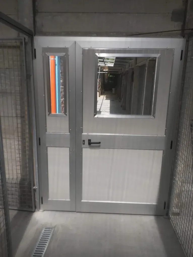 Porta metallica con finestra e pannello adiacente, in un corridoio con lati ingabbiati.