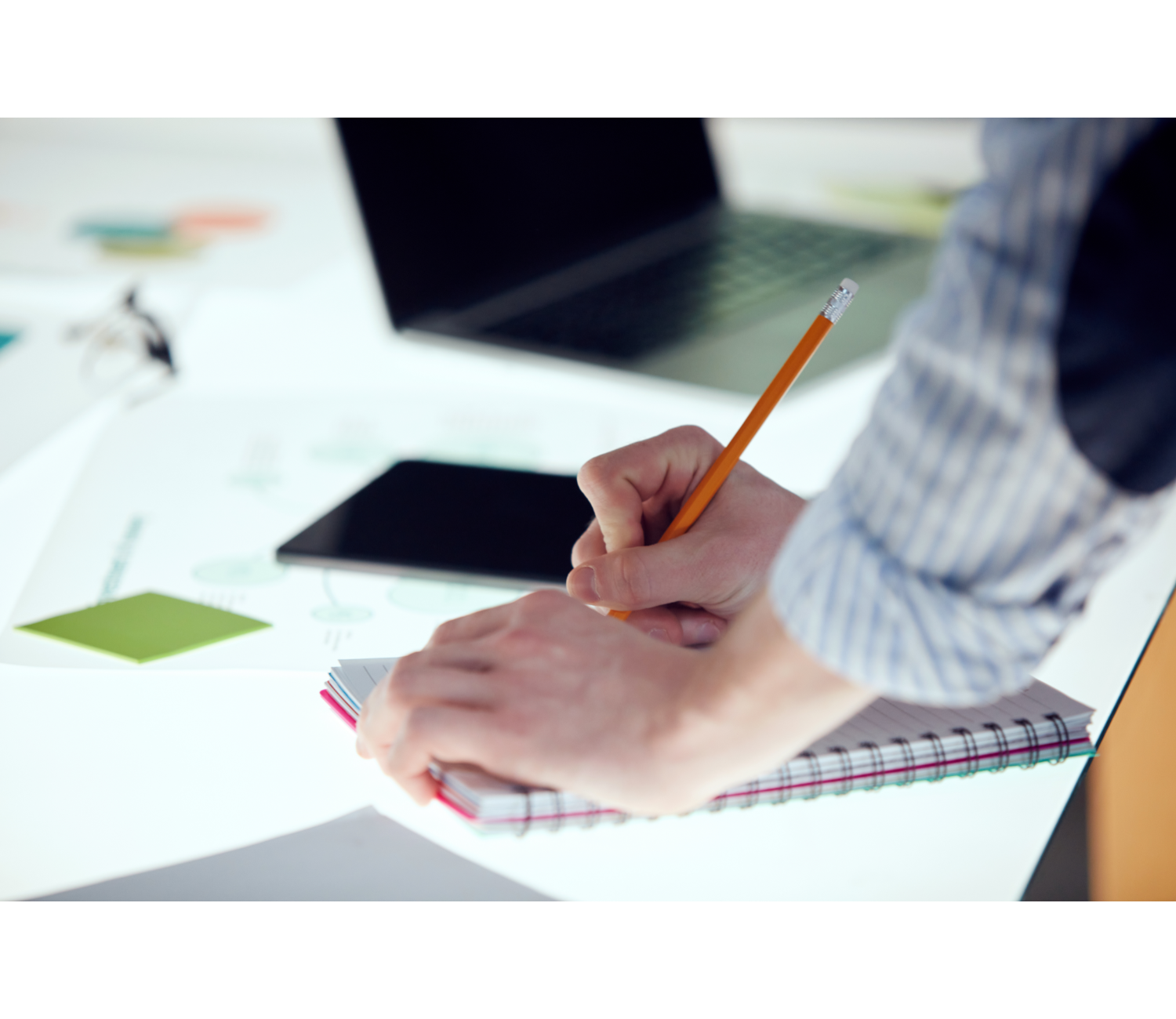 Eine Person schreibt mit einem Bleistift in ein Notizbuch.