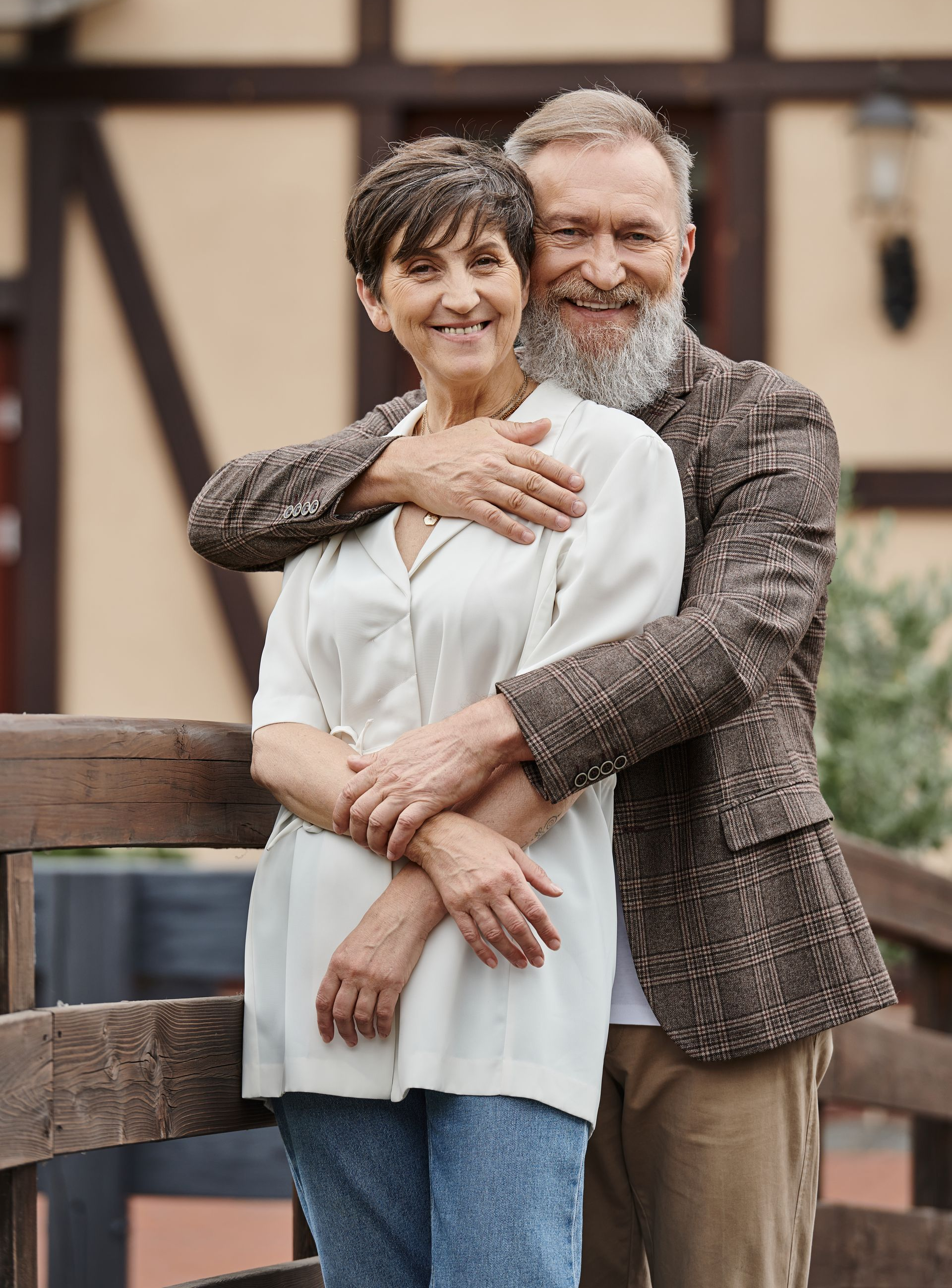 Couple embracing outdoors; woman in white top, man in tweed jacket, smiling.
