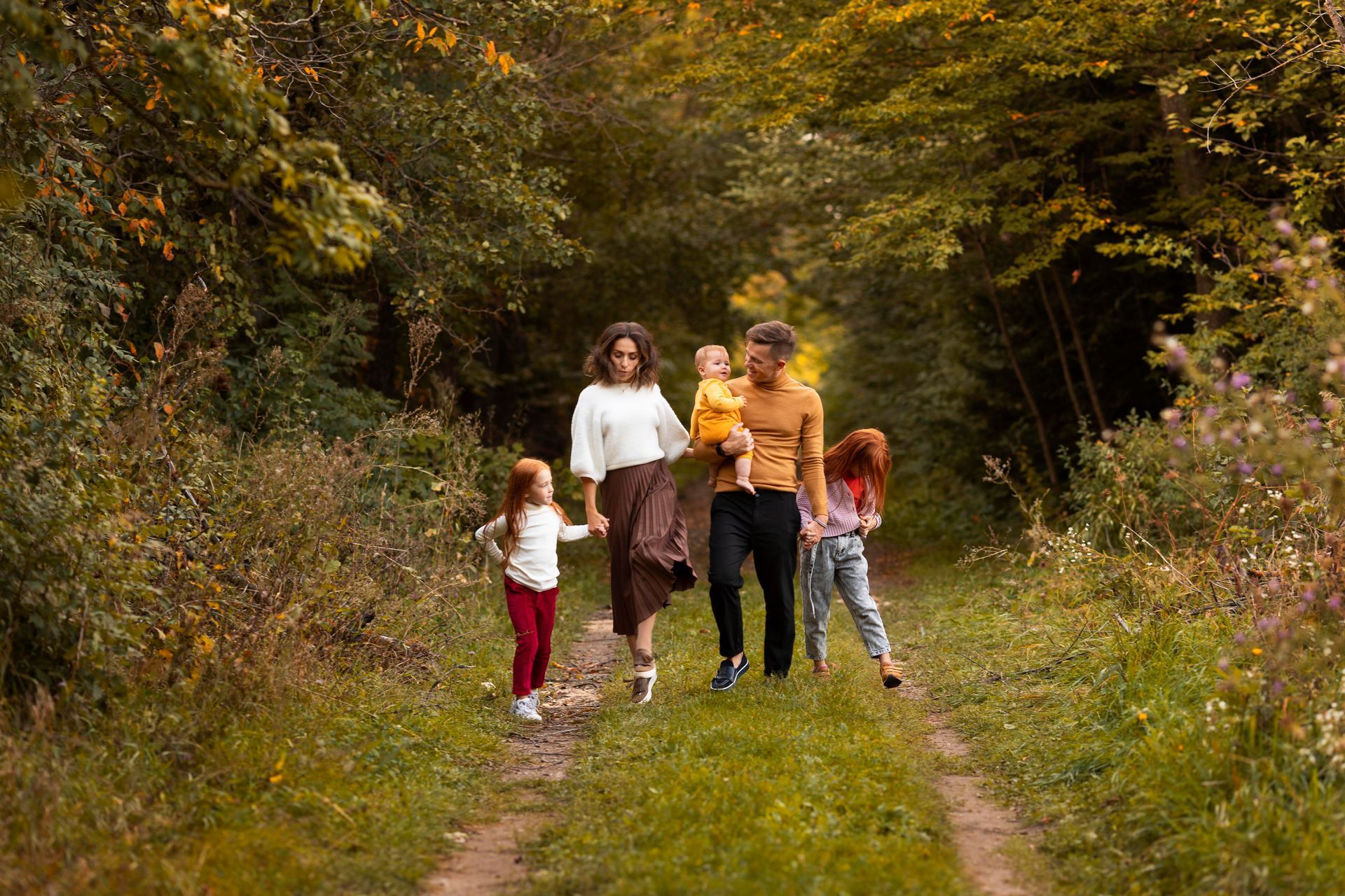 Family walking on a path through a wooded area; two adults and three children.