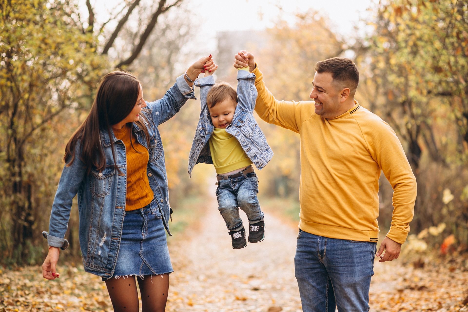 Parents holding a child up in the air on a path in autumn, all smiling.
