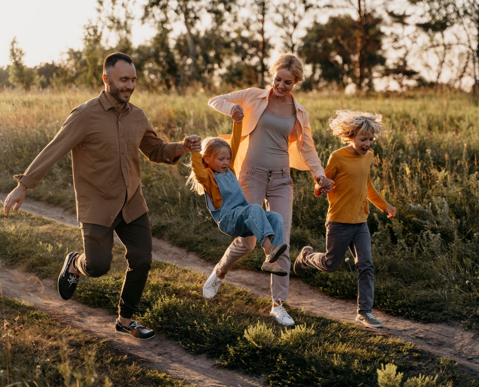 Family running through a field, holding hands. The sun shines brightly.